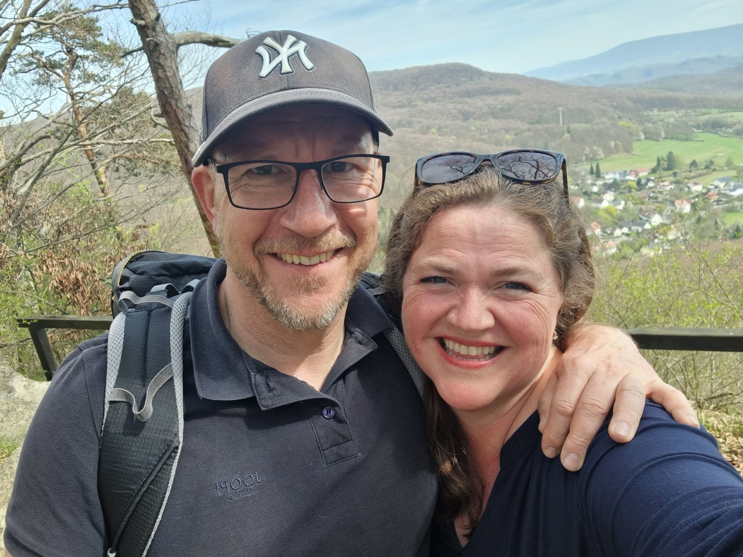 Kandace Blevin and her partner Klaus smiling outdoors above a village and wooded hills in Meinhard, Germany.